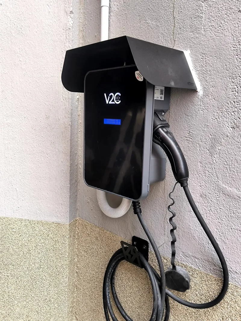 Punto de carga de coche eléctrico con visera protectora en la esquina de una fachada
