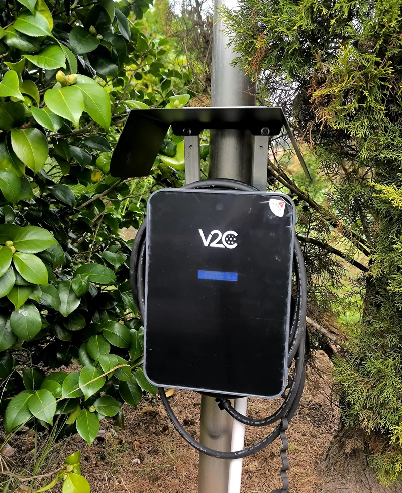 Cargador de vehículo eléctrico con visera protectora instalado en un poste del jardín