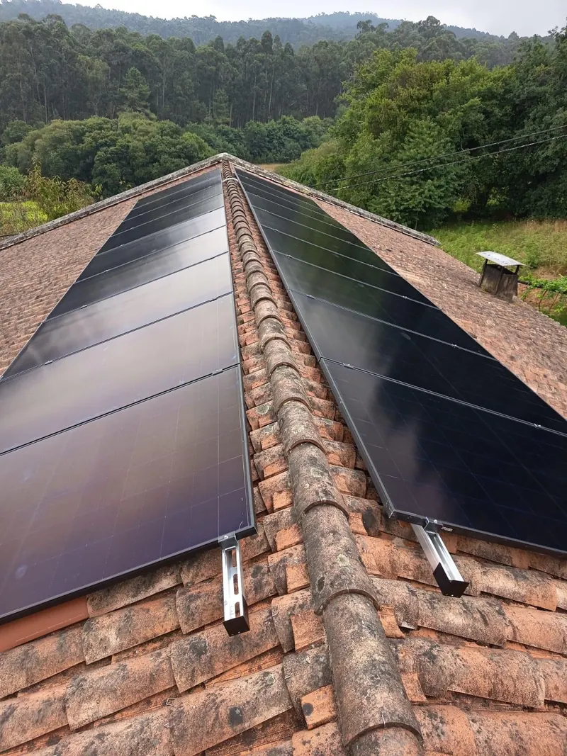 Paneles fotovoltaicos a ambos lados de la cumbrera con bosque de fondo