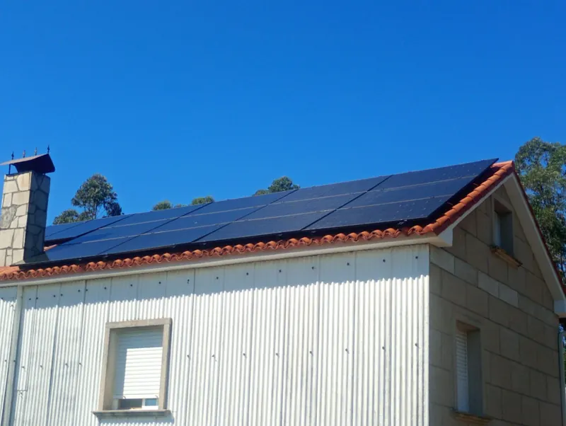 Instalación fotovoltaica sobre el tejado de una vivienda con paredes de granito y chapa