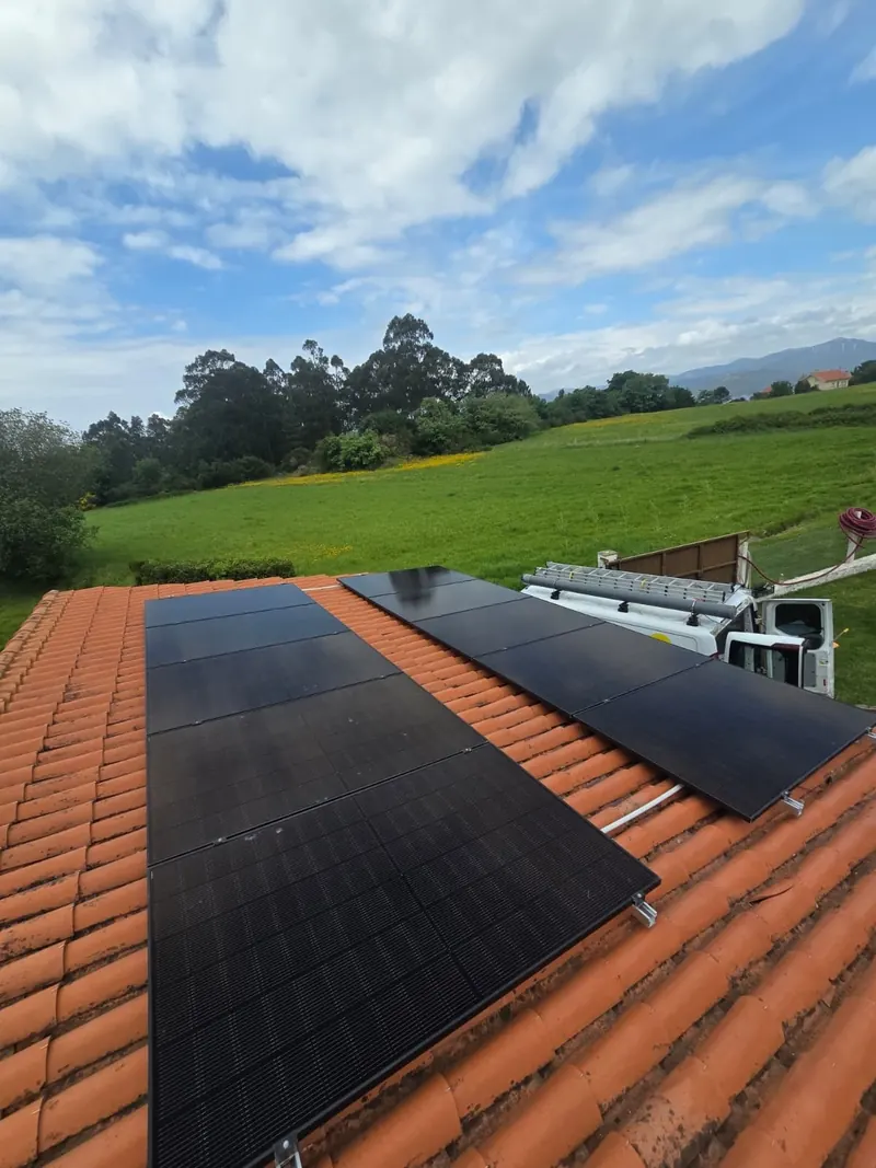 Paneles solares negros sobre tejado de teja con prado y furgoneta de instalación